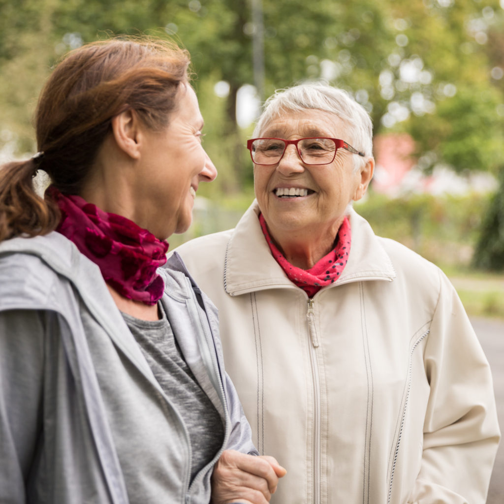 Happy senior woman and caregiver walking outdoors
